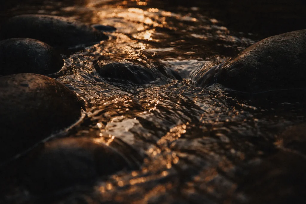 eau qui s’écoule sur des pierres sombres lumière dorée mouvement lent symbole du rapport à l’argent et des émotions