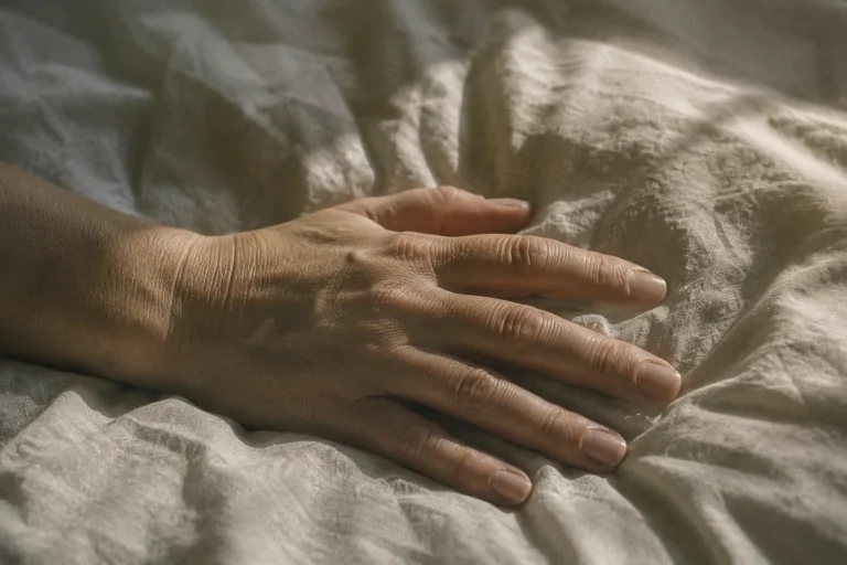 Main immobile posée sur un drap froissé au petit matin — premiers signaux physiques d’un burn-out et épuisement silencieux
