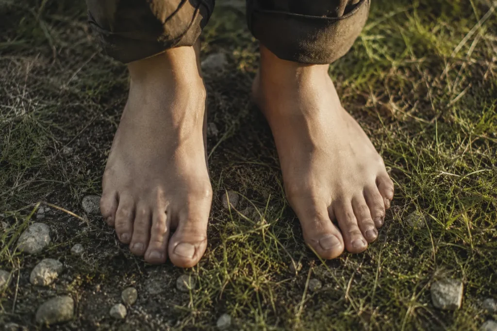 Pieds nus posés sur la terre et l’herbe dans une lumière douce — retour au corps après épuisement et signaux burn-out